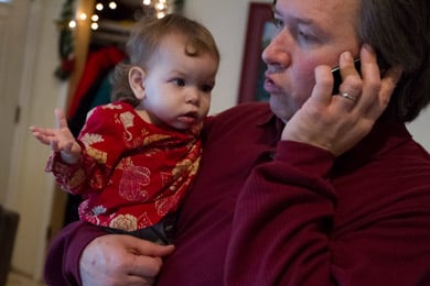 Willie Rembis talks on the phone while holding his daughter Cora. (Jeffrey Sauger for ProPublica)