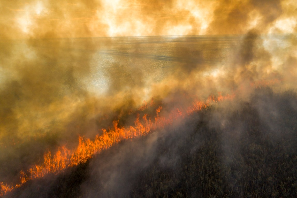 A line of fire cuts across a field. The whole image is heavily obscured by smoke.
