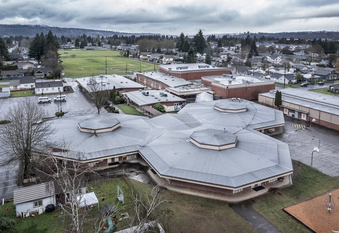 An overhead view of a school campus featuring three octagonal buildings in the foreground, sports fields and mountains in the background.