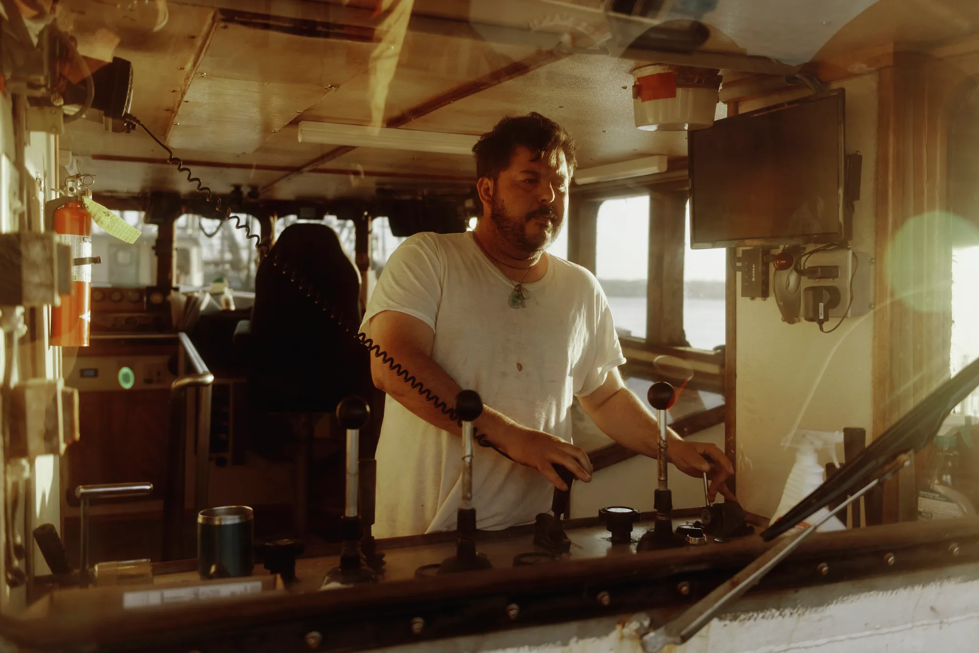 A bearded man in a white T-shirt operates a panel of levers.