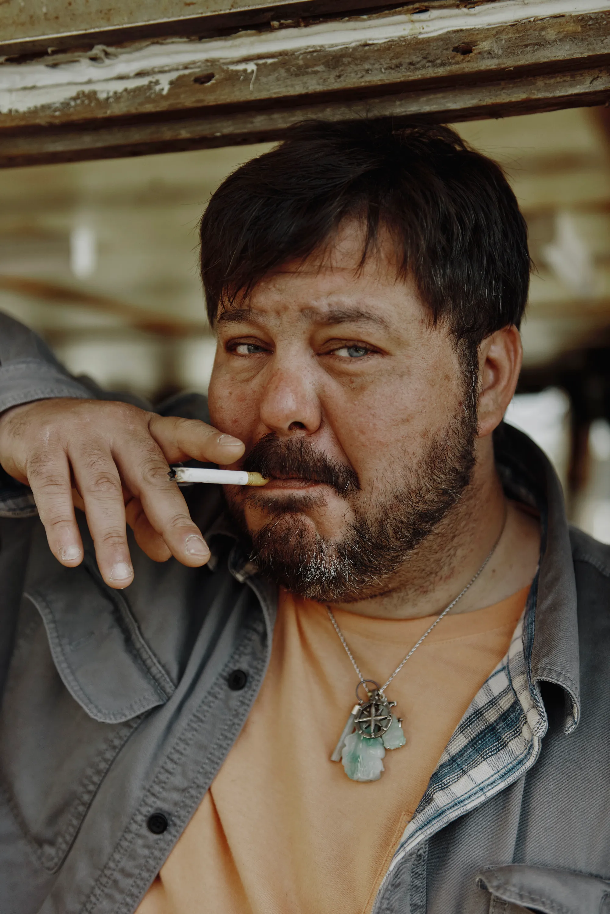 Leeman smokes a cigarette. His necklace, with its compass and pieces of jade, is visible.