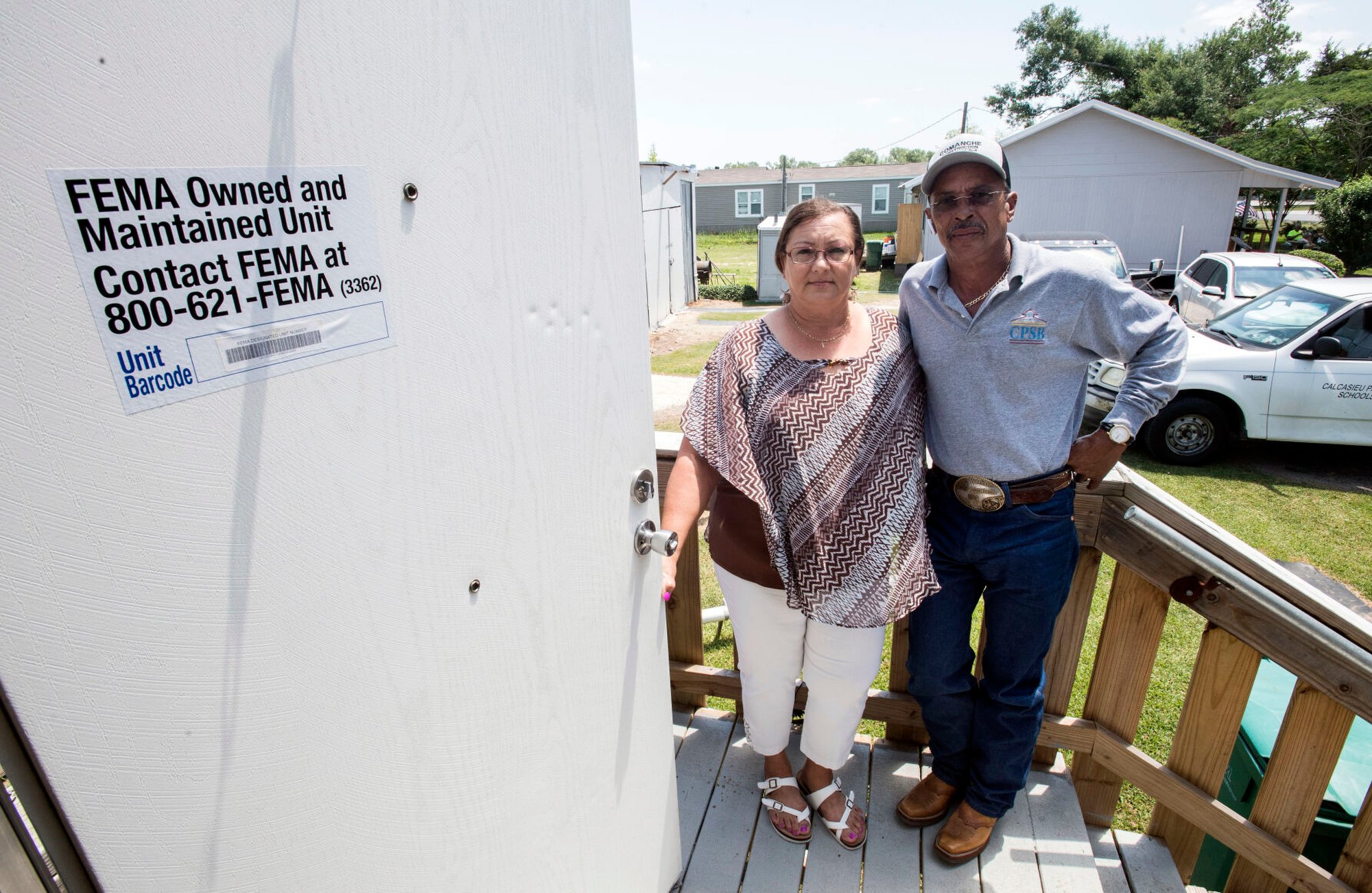 A couple stand outside on wooden steps next to a door with a sign that says 