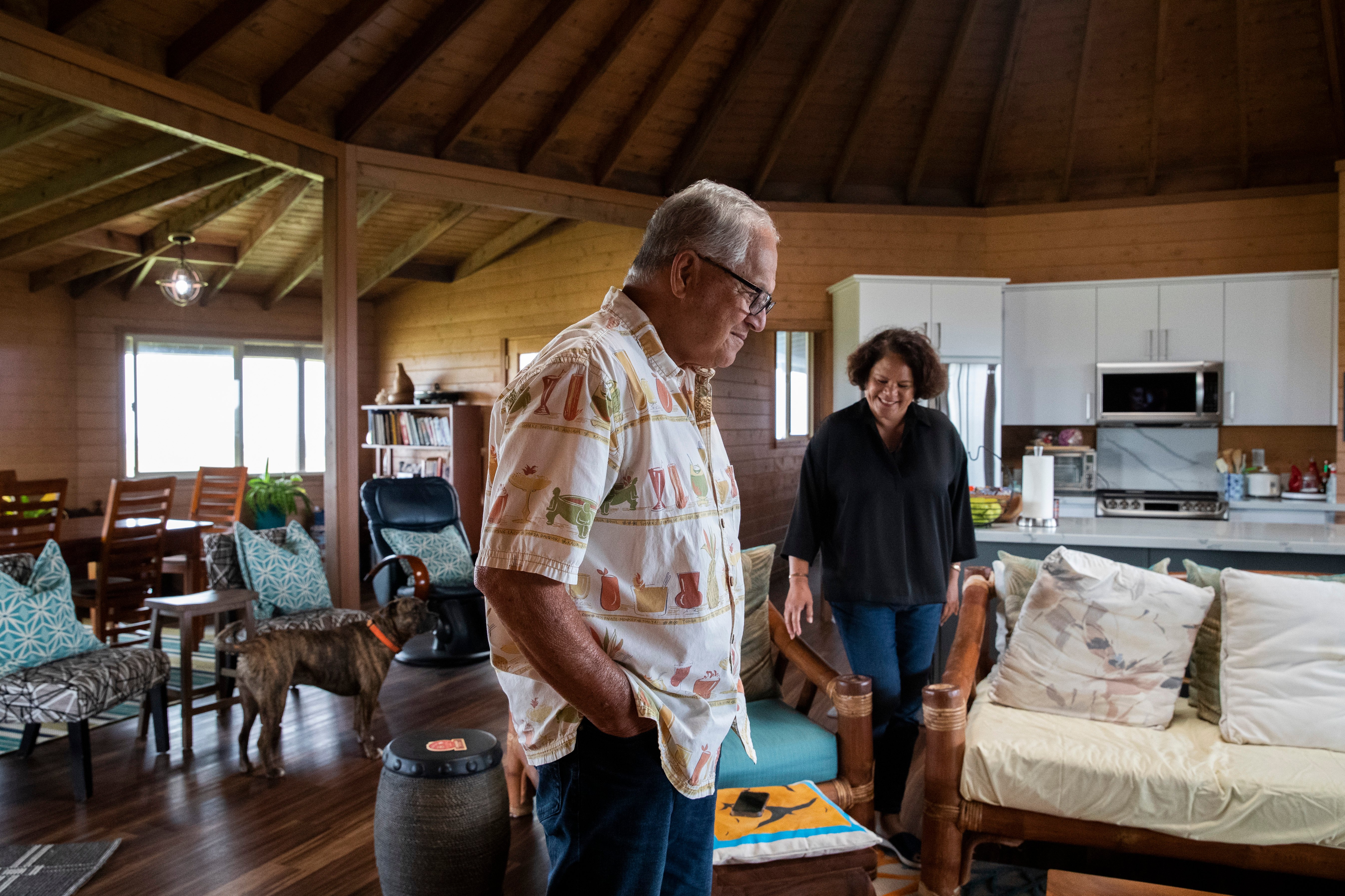 A man and woman stand in a large, well-furnished living/dining area, with a dog nearby.