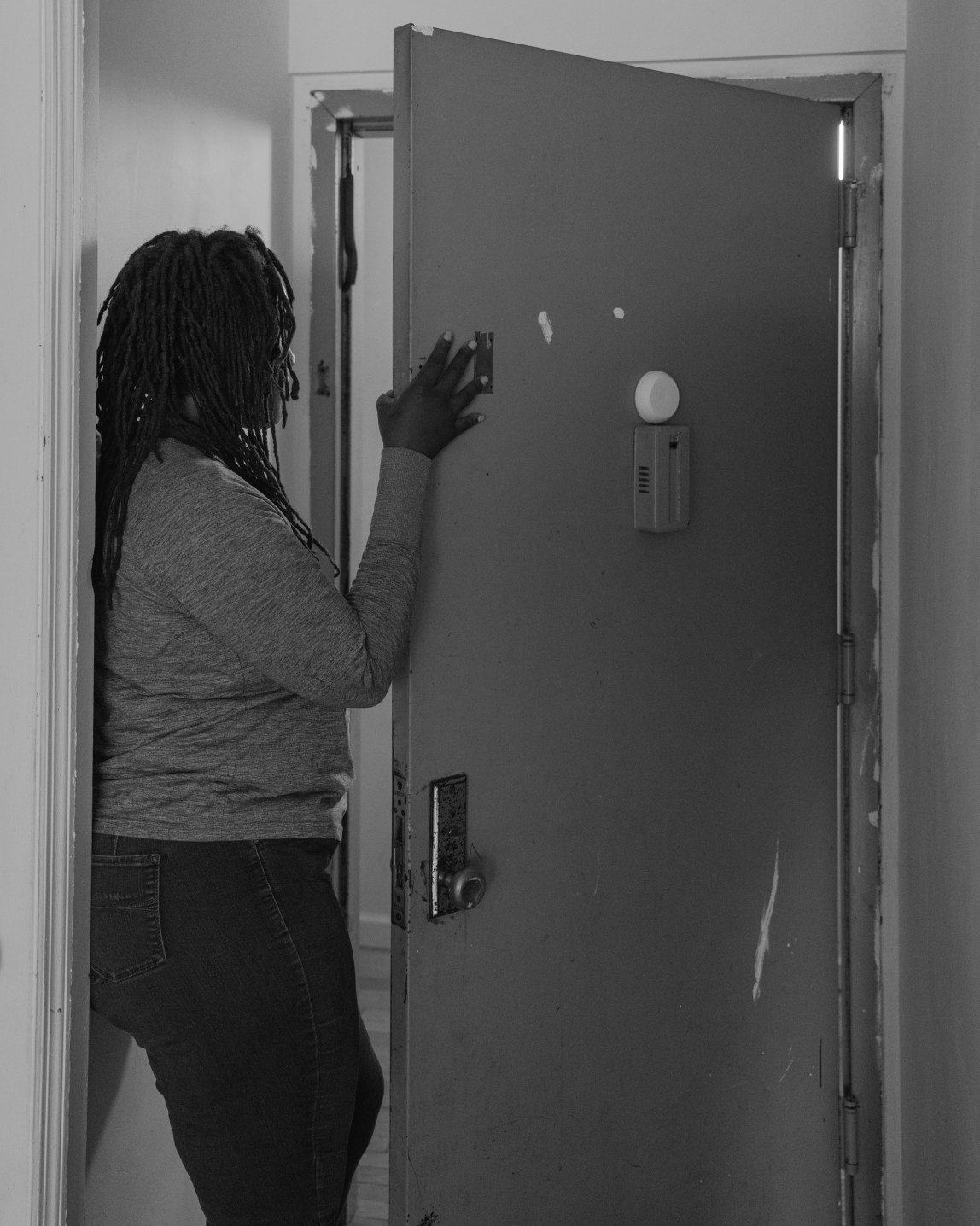 A Black woman, seen from inside her home, stands in the partially open front door.