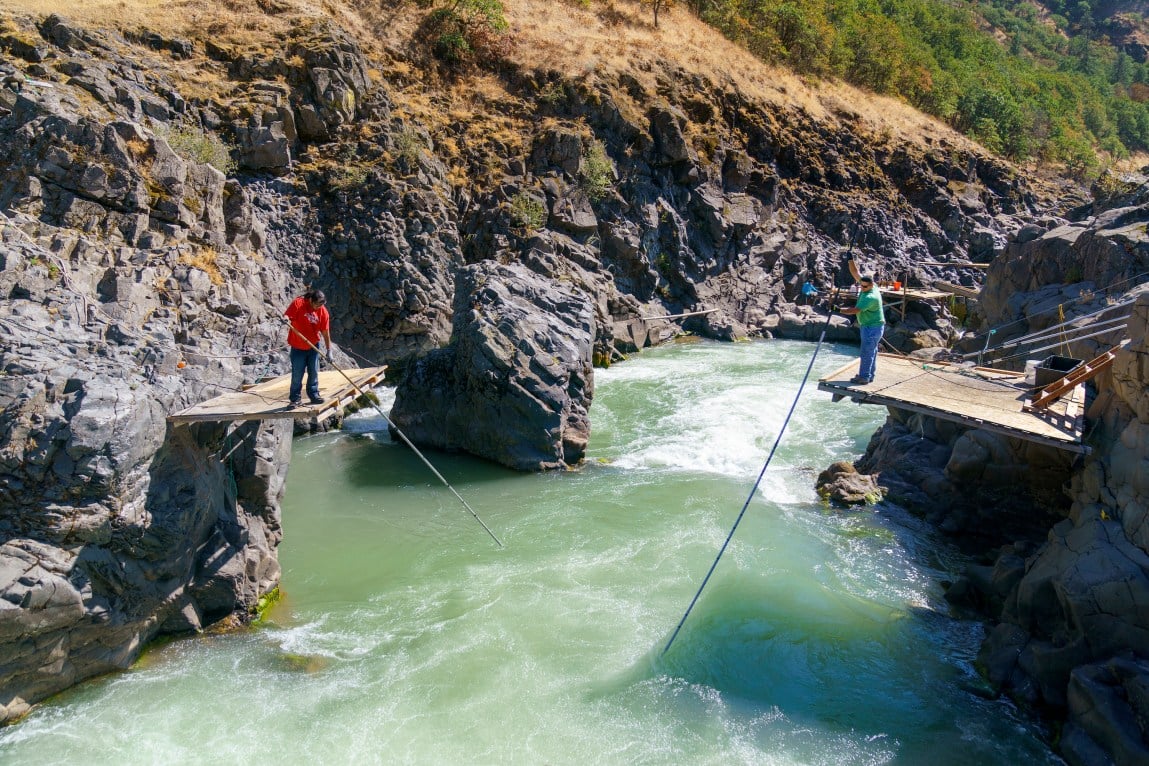 Two people hold a net from opposite sides of a surging river.