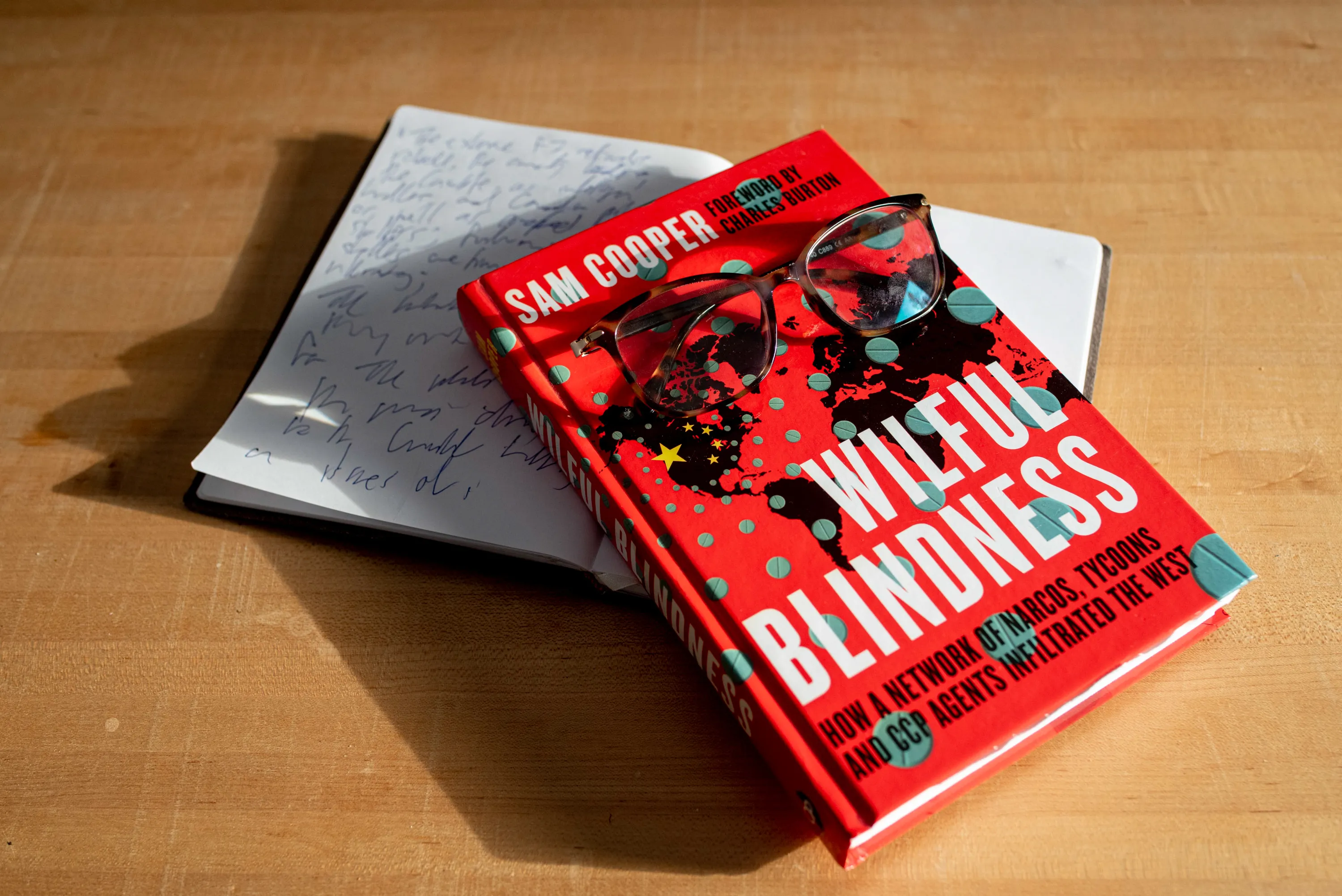 An open notebook and a book with a pair of glasses sitting atop them.