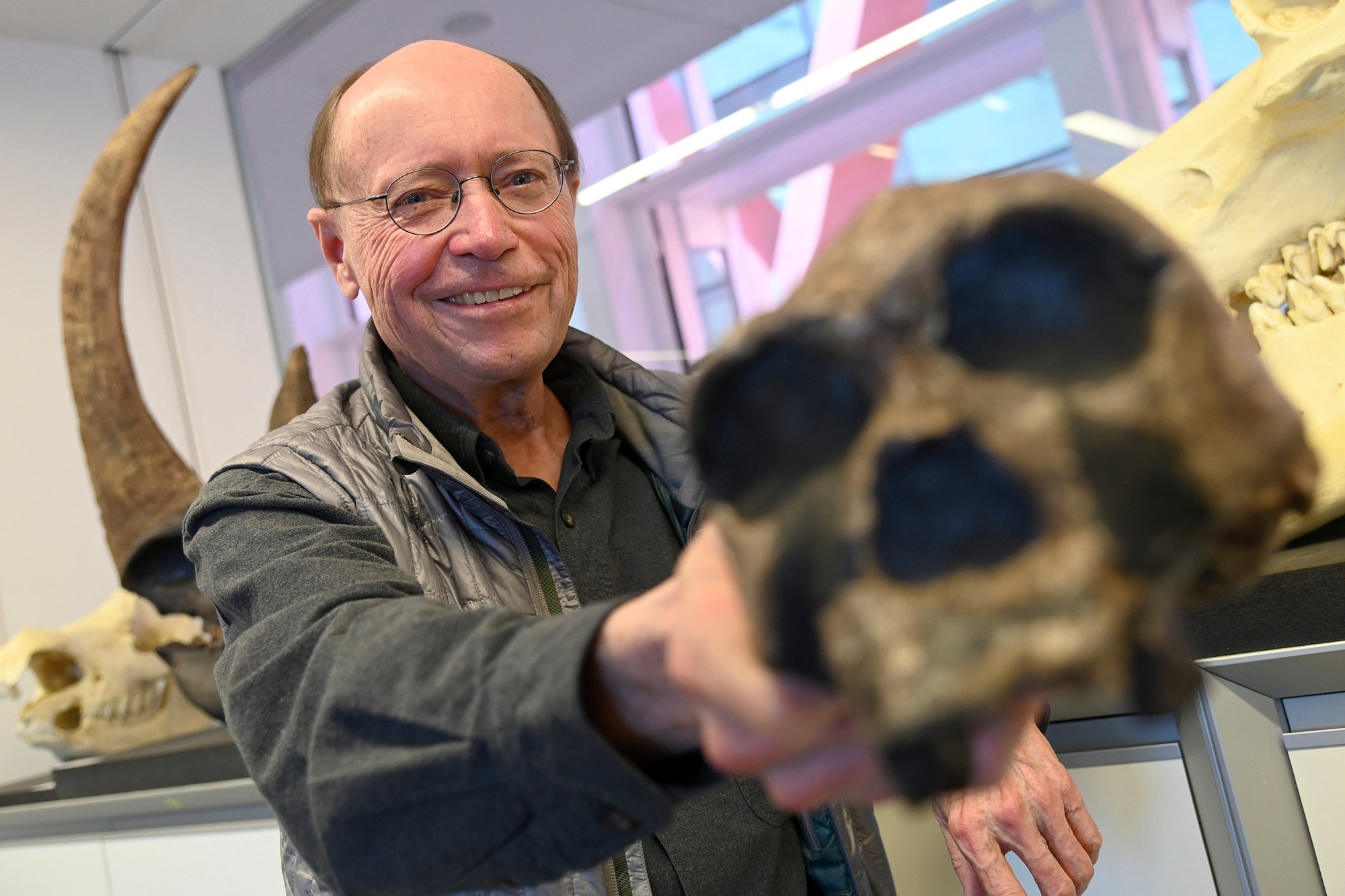 A man holds a hominid skull up to the camera.