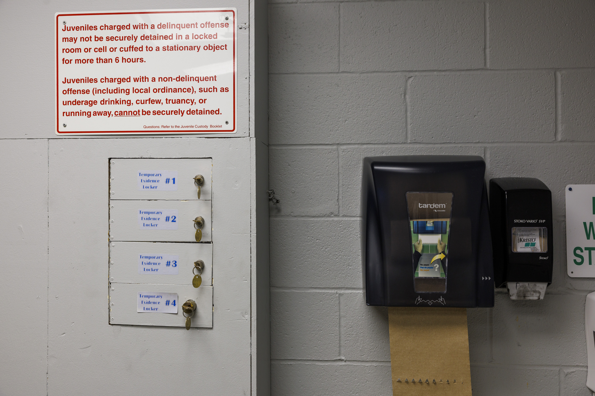 A sign with detention instructions and a set of lockers are mounted to a cinderblock wall near a paper towel dispenser.