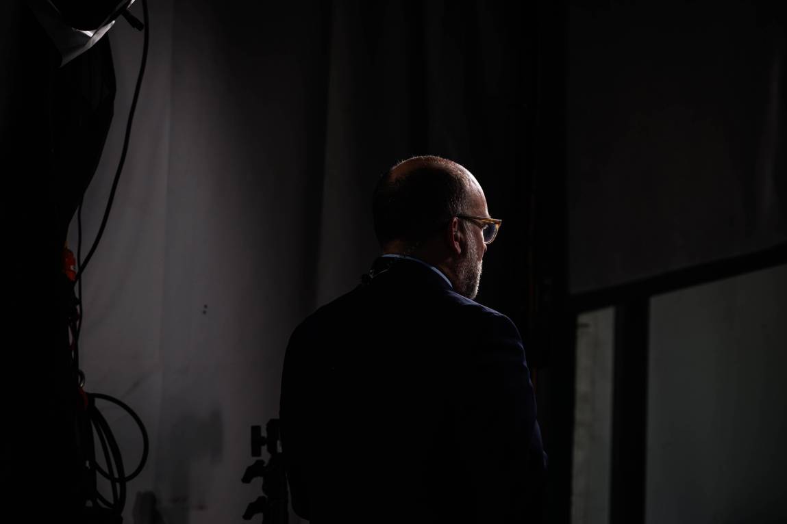 Vought, seen from behind, standing in shadows.