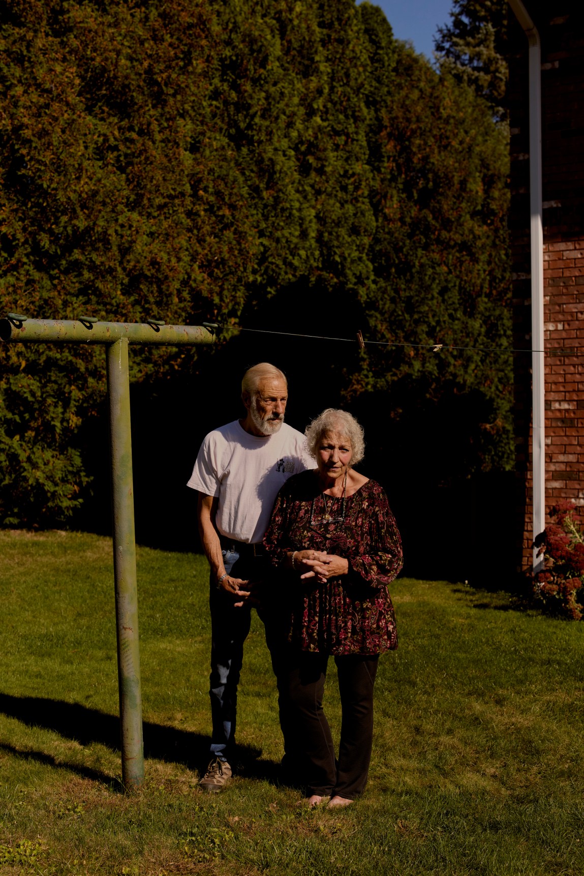 An older couple stand alongside a clothesline in a residential back yard.